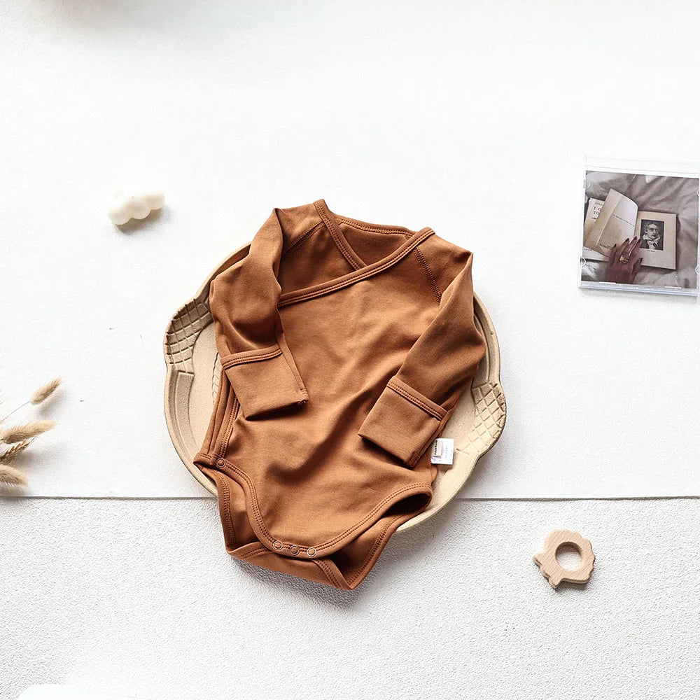 Brown baby long sleeve bodysuit laid in a brown tray in an aesthetic light gray background