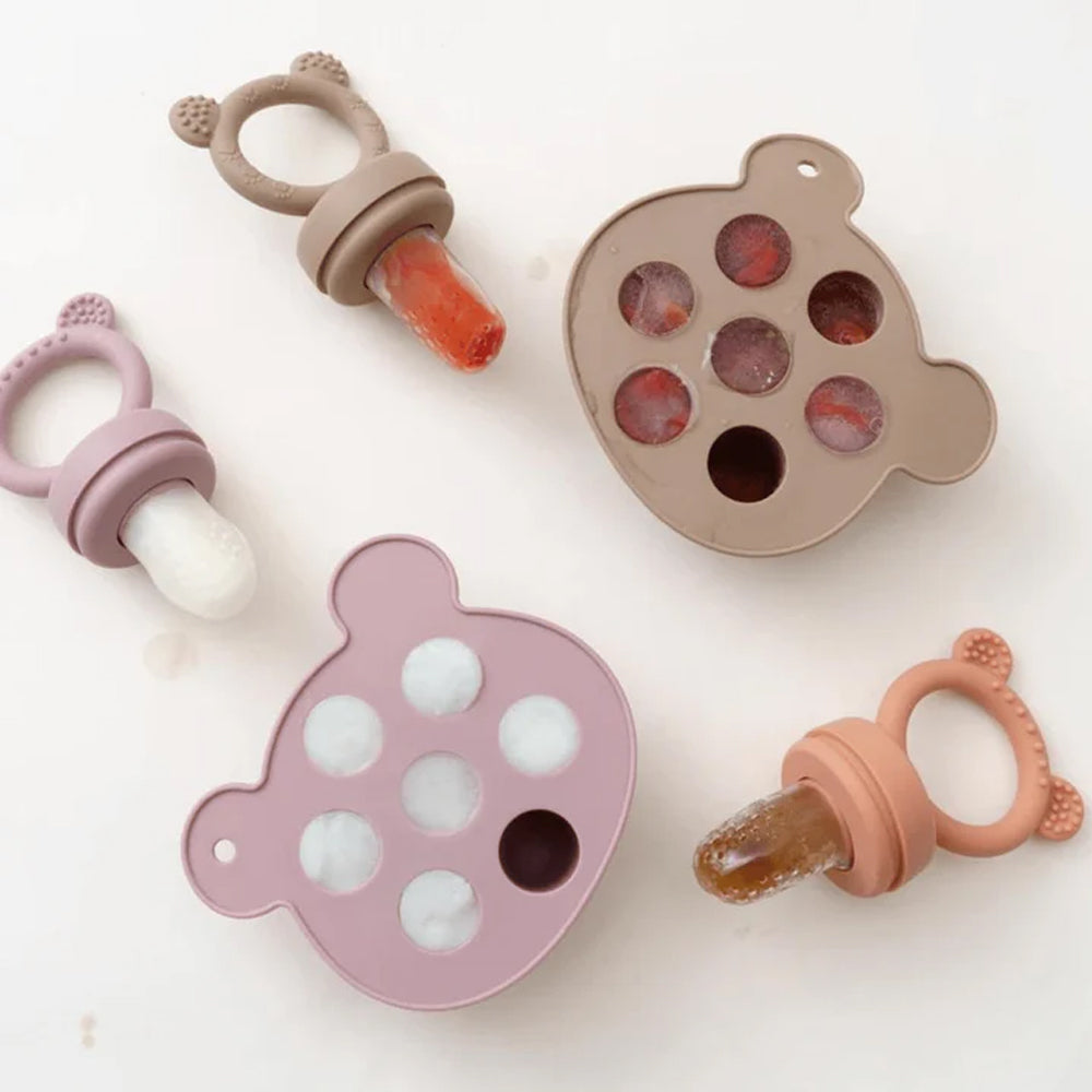 Baby teething toys and pacifiers with frozen fruit on a light background.