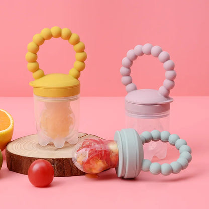 Three colorful baby fruit feeders on a pink background.