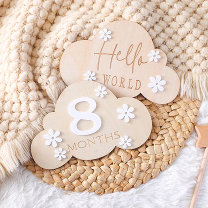 A cloud shaped wooden milestone card displaying Hello World alongside another card displaying 8 months, set against a soft, neutral aesthetic background