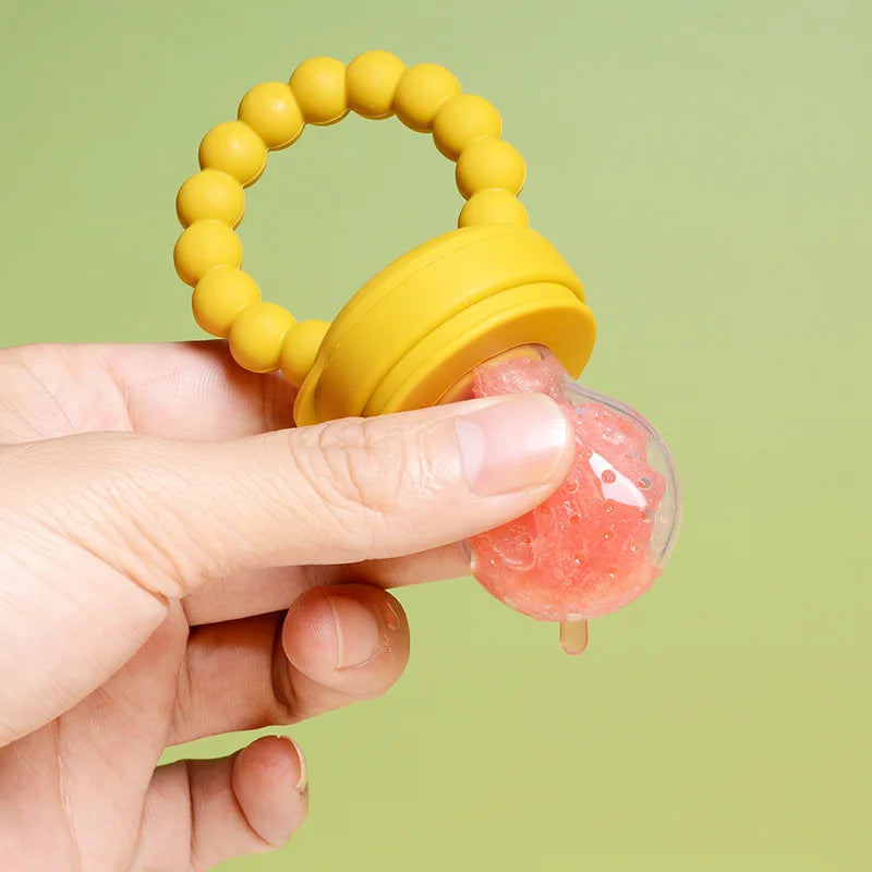 A hand holding a yellow baby teething toy with pink gel on a green background.