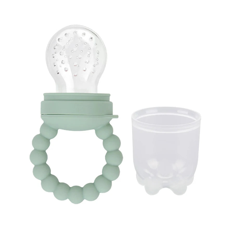 Silicone baby teether with bead ring and detachable white top next to a transparent cup.
