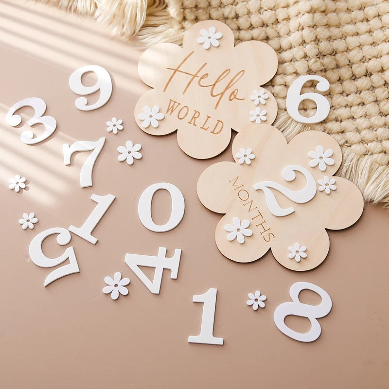 A flower shaped wooden milestone card displaying Hello World alongside another card displaying 2 months, in an aesthetic background with white flower and number cutouts