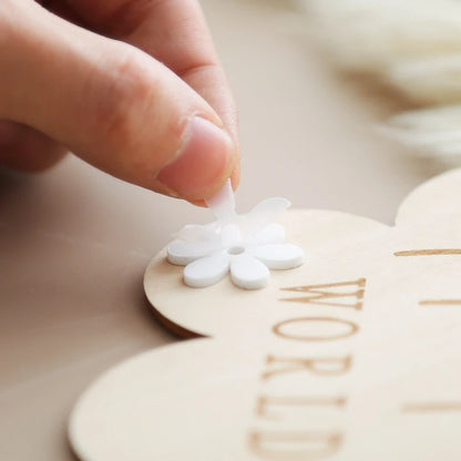 A person attaching a flower cutout to a wooden milestone card