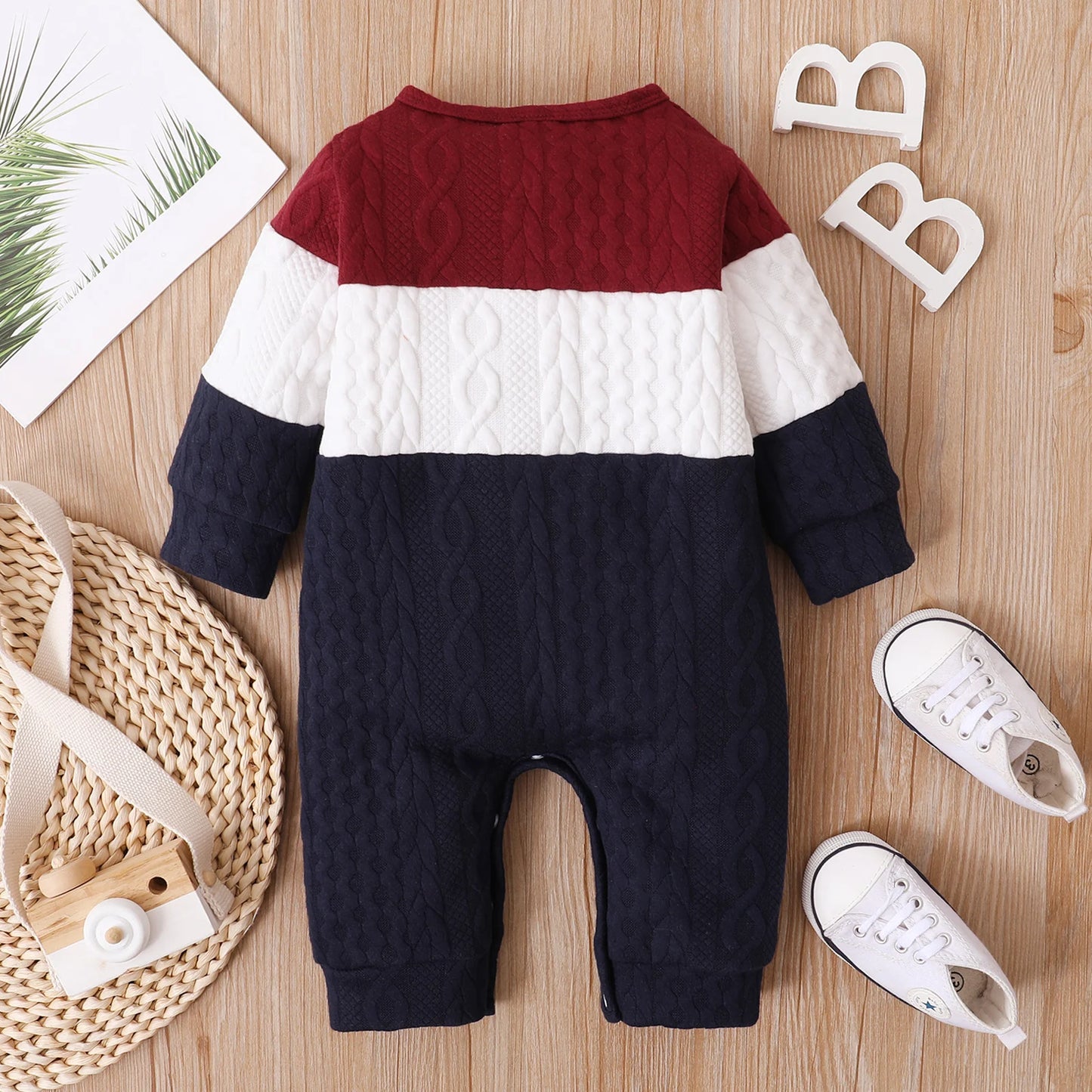 Red, White, and Navy Blue Colorblock, Cable Knit Baby Jumpsuit Romper Laid In A Light Wooden Background Alongside a White Shoes And Photoprops