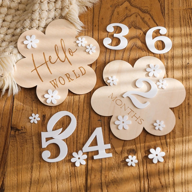  A cloud shaped wooden milestone card displaying Hello World alongside another card displaying 2 months, set against a wooden background with white flower and number cutouts